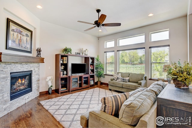 living room featuring a fireplace, ceiling fan, and dark wood-type flooring