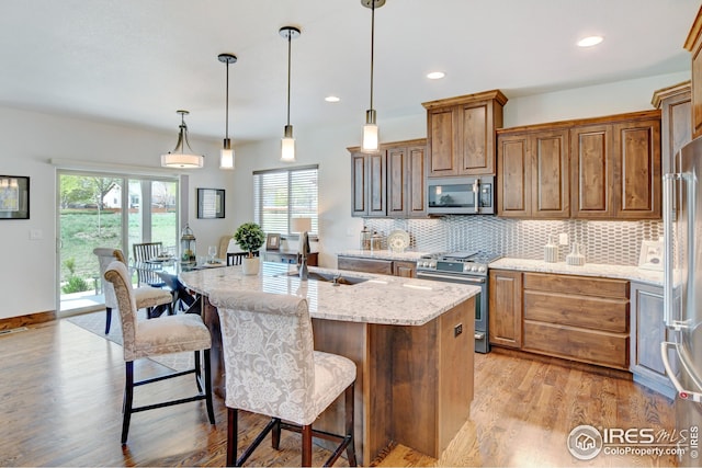 kitchen featuring pendant lighting, sink, light stone countertops, an island with sink, and appliances with stainless steel finishes