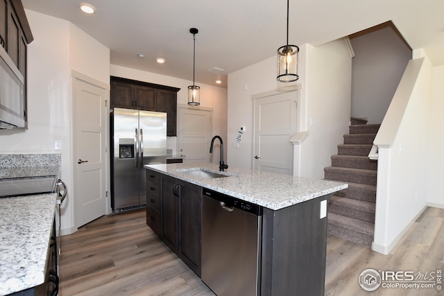 kitchen with stainless steel appliances, sink, decorative light fixtures, light hardwood / wood-style flooring, and a center island with sink