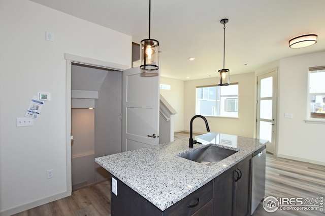 kitchen featuring light stone counters, stainless steel dishwasher, sink, decorative light fixtures, and an island with sink