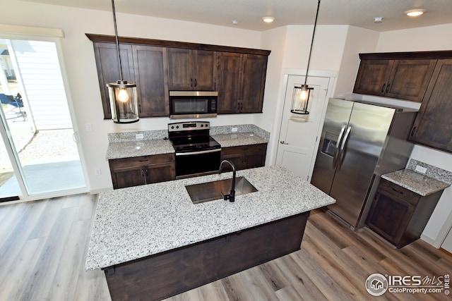 kitchen with light stone countertops, appliances with stainless steel finishes, hanging light fixtures, and sink