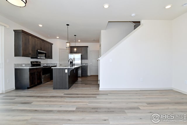 kitchen featuring appliances with stainless steel finishes, a breakfast bar, dark brown cabinetry, decorative light fixtures, and an island with sink