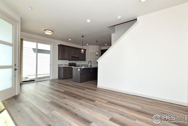 kitchen featuring pendant lighting, a kitchen island with sink, a kitchen breakfast bar, light wood-type flooring, and dark brown cabinetry