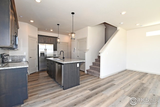 kitchen featuring sink, an island with sink, appliances with stainless steel finishes, decorative light fixtures, and light stone counters