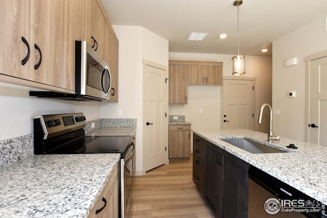 kitchen featuring light stone countertops, light hardwood / wood-style flooring, hanging light fixtures, appliances with stainless steel finishes, and sink