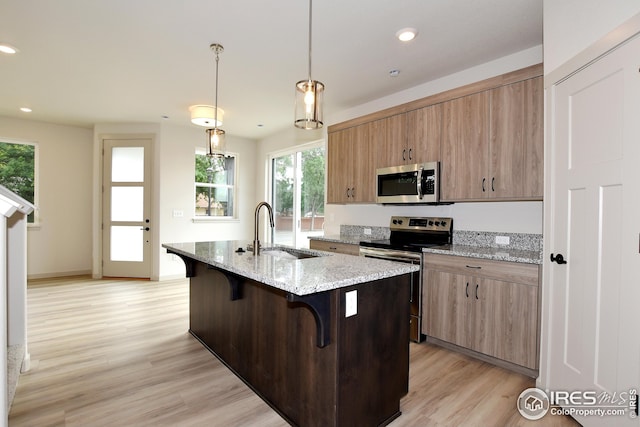 kitchen with a kitchen breakfast bar, stainless steel appliances, an island with sink, sink, and decorative light fixtures