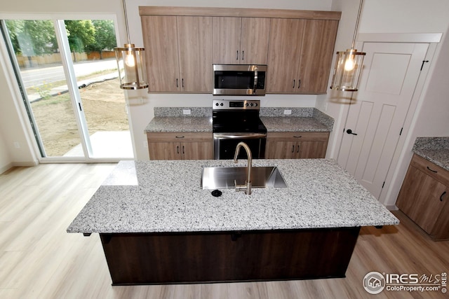 kitchen with stainless steel appliances, sink, light hardwood / wood-style floors, light stone countertops, and a kitchen island with sink