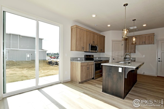 kitchen featuring a center island with sink, stainless steel appliances, light stone countertops, pendant lighting, and sink