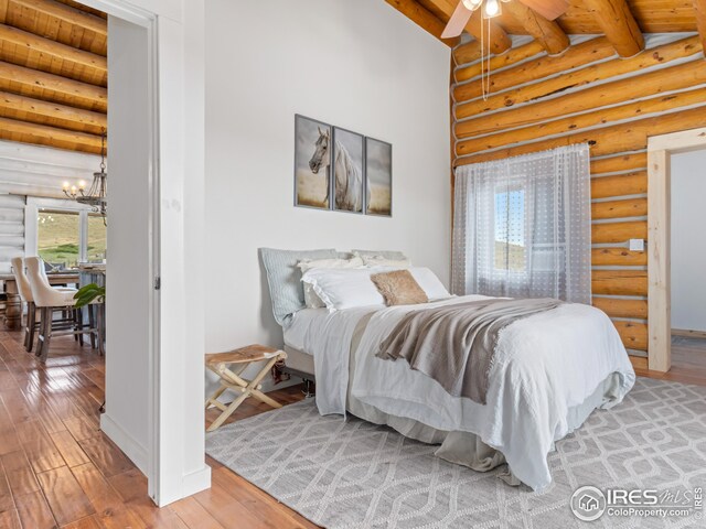 bedroom featuring vaulted ceiling with beams, light wood-type flooring, ceiling fan with notable chandelier, wood ceiling, and rustic walls