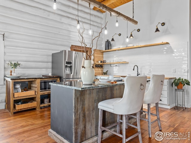 kitchen with light hardwood / wood-style floors, black microwave, dark stone counters, rustic walls, and stainless steel fridge