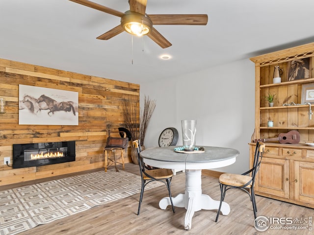 dining area with ceiling fan, wooden walls, and light hardwood / wood-style flooring