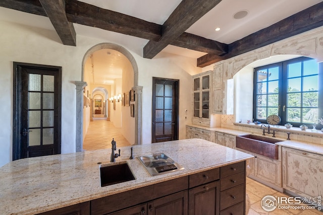 kitchen with dark brown cabinetry, sink, light stone counters, and beam ceiling