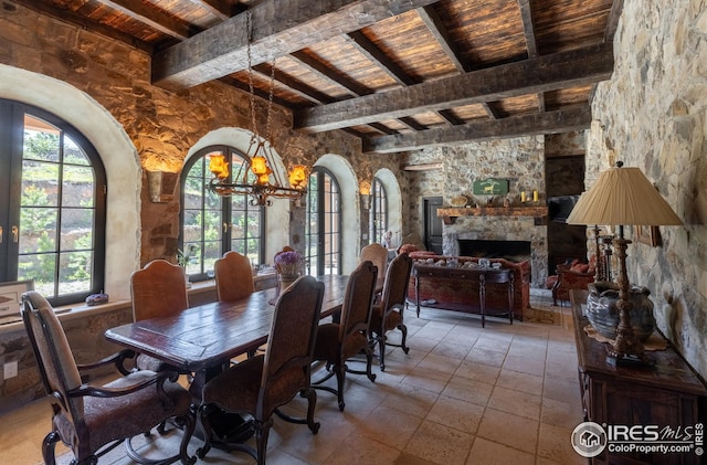 dining space featuring a stone fireplace, beam ceiling, tile patterned flooring, a chandelier, and wooden ceiling