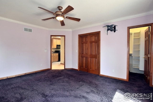 unfurnished bedroom with dark colored carpet, crown molding, a spacious closet, and ceiling fan