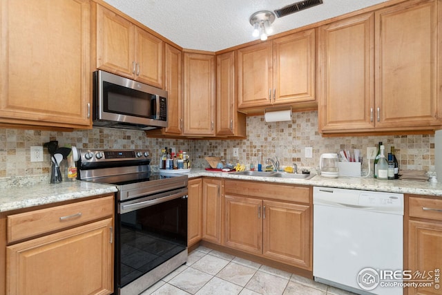 kitchen with sink, backsplash, stainless steel appliances, light stone countertops, and a textured ceiling