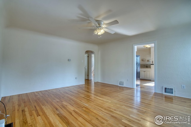 unfurnished room with arched walkways, light wood finished floors, and visible vents