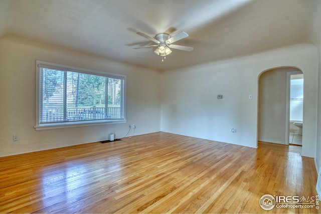 unfurnished room featuring a ceiling fan, arched walkways, and wood finished floors