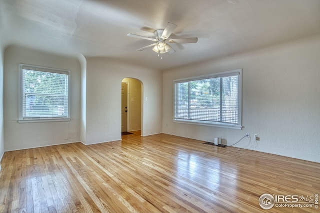 empty room featuring a ceiling fan, arched walkways, and wood finished floors