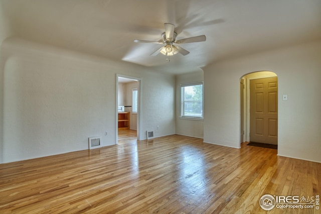 unfurnished room featuring light wood-type flooring, visible vents, and arched walkways