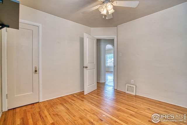 spare room with a ceiling fan, arched walkways, visible vents, and light wood finished floors