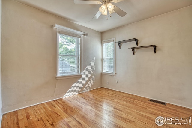empty room with wood finished floors, visible vents, and a ceiling fan