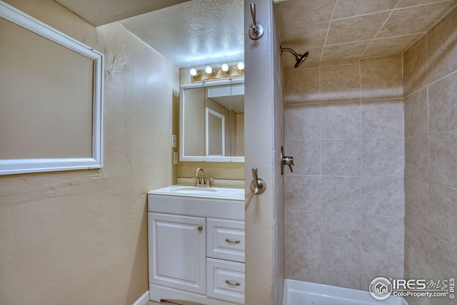bathroom featuring a textured wall, a tile shower, and vanity