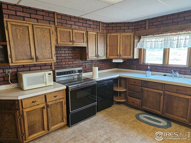 kitchen featuring a paneled ceiling, brick wall, sink, and black appliances