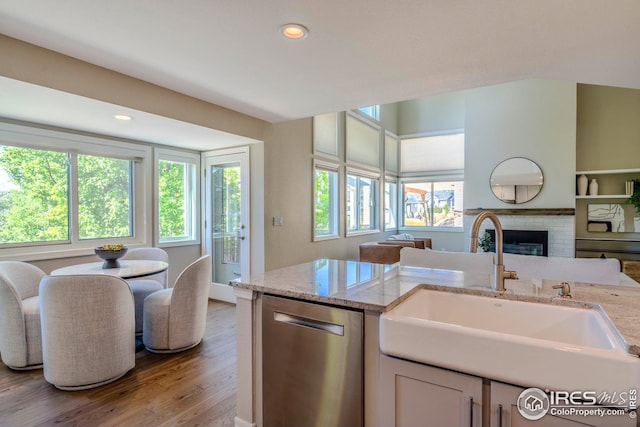 kitchen with sink, stainless steel dishwasher, light hardwood / wood-style flooring, white cabinetry, and light stone countertops