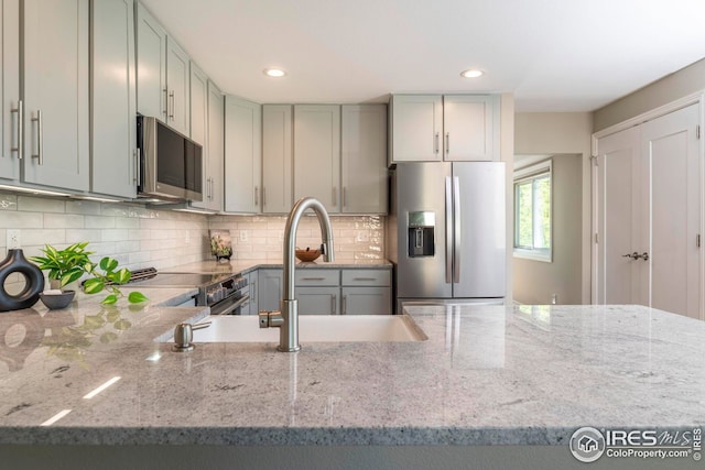 kitchen featuring light stone counters, gray cabinets, stainless steel appliances, and tasteful backsplash