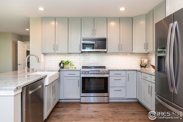 kitchen featuring appliances with stainless steel finishes, kitchen peninsula, light stone countertops, dark hardwood / wood-style floors, and sink