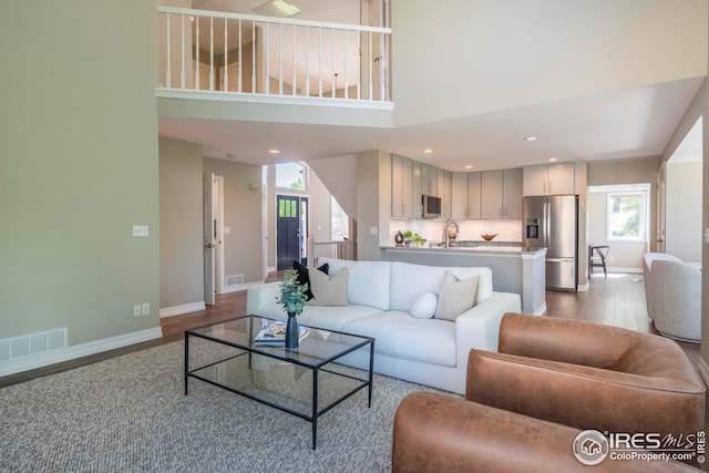 living room with sink, a towering ceiling, light hardwood / wood-style floors, and a healthy amount of sunlight