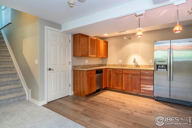 kitchen with light stone countertops, pendant lighting, stainless steel appliances, light hardwood / wood-style flooring, and sink