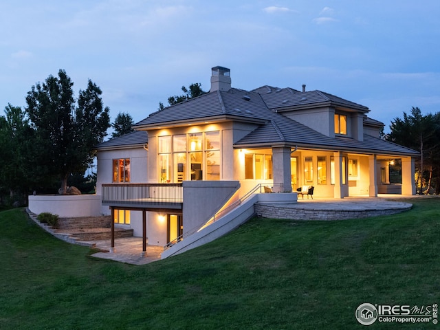 back house at dusk featuring a lawn and a patio