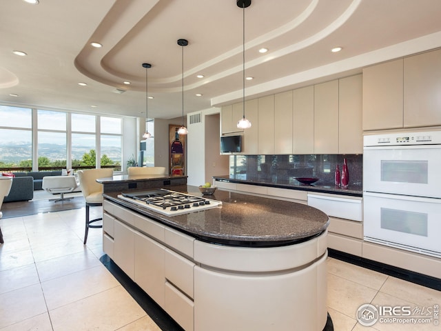 kitchen featuring a raised ceiling, stainless steel gas cooktop, white double oven, and decorative backsplash