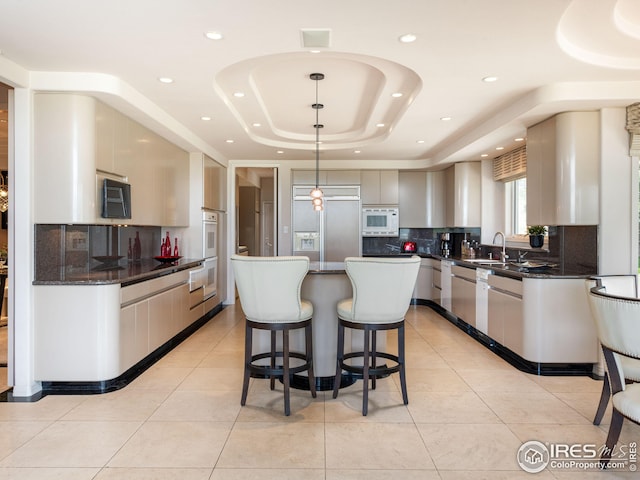 kitchen with built in appliances, backsplash, a kitchen island, a tray ceiling, and light tile patterned flooring