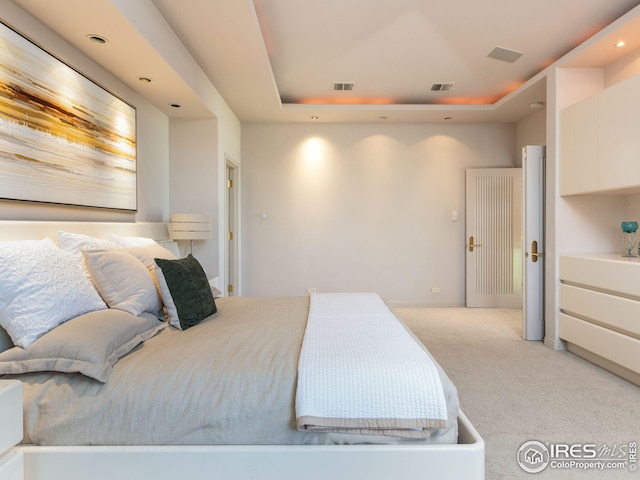 bedroom with a raised ceiling and light colored carpet