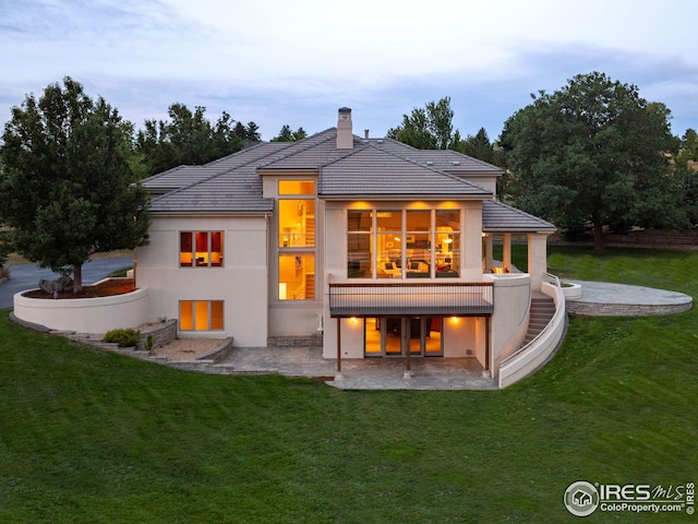 back house at dusk featuring a lawn and a patio