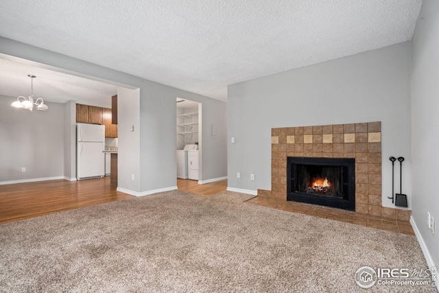 unfurnished living room featuring light hardwood / wood-style floors, a textured ceiling, an inviting chandelier, washing machine and dryer, and a tile fireplace