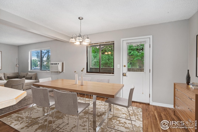 dining area with a wall unit AC, wood-type flooring, a notable chandelier, and a textured ceiling