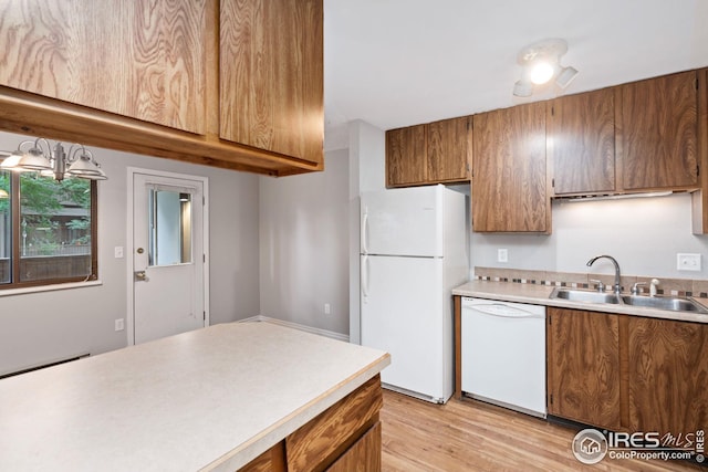 kitchen featuring a notable chandelier, sink, pendant lighting, light hardwood / wood-style flooring, and white appliances