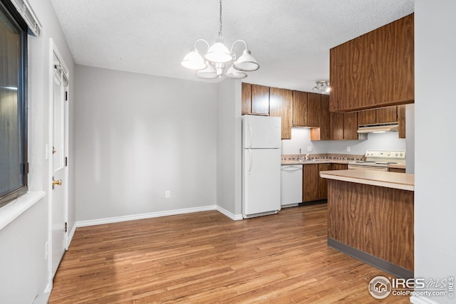 kitchen featuring hanging light fixtures, a chandelier, a textured ceiling, light hardwood / wood-style flooring, and white appliances