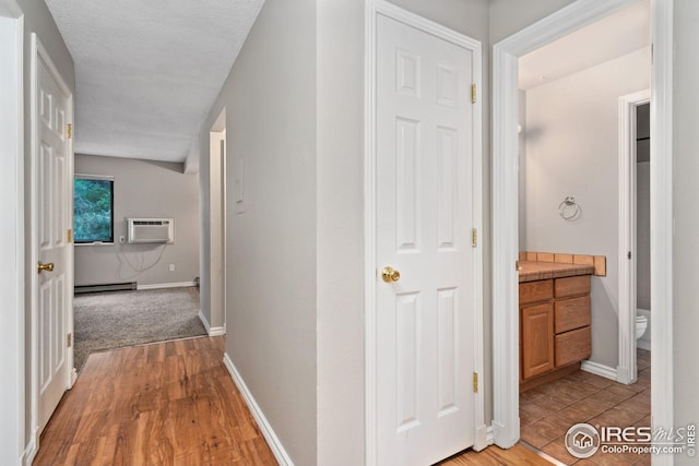 corridor featuring a textured ceiling, an AC wall unit, light hardwood / wood-style flooring, and a baseboard heating unit