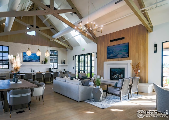 living room featuring wood finished floors, a chandelier, beam ceiling, and a glass covered fireplace