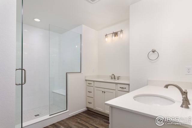 bathroom with a stall shower, two vanities, a sink, and wood finished floors