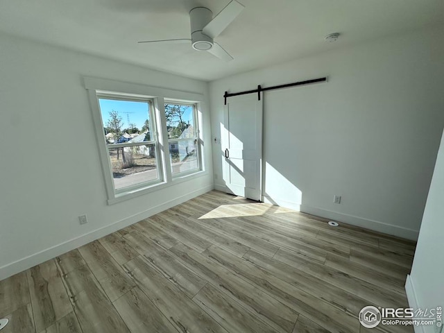 unfurnished room with a barn door, light wood-type flooring, and ceiling fan