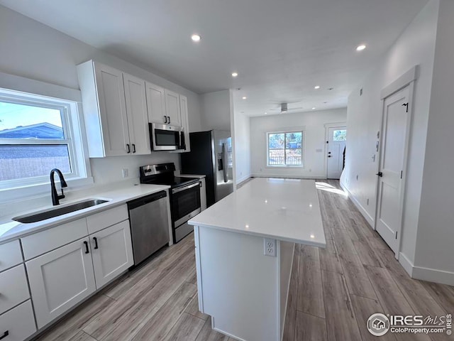 kitchen featuring a kitchen island, stainless steel appliances, sink, light wood-type flooring, and white cabinetry