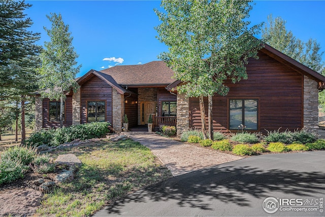 view of front of property with a shingled roof, stone siding, and covered porch