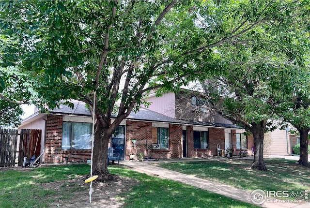 view of front of home featuring brick siding, fence, and a front lawn