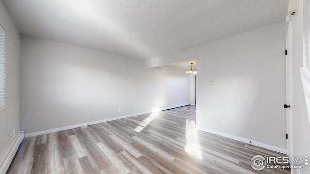 empty room with baseboard heating, light hardwood / wood-style floors, a textured ceiling, and a notable chandelier