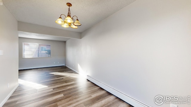 empty room with wood-type flooring, a textured ceiling, a baseboard radiator, and an inviting chandelier